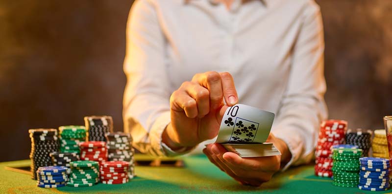 Djevojka krupje drži karte u rukama. Mnogo je šarenih žetona na zelenoj tkanini kockarskog stola. Casino, poker, kockanje, strategija igre.